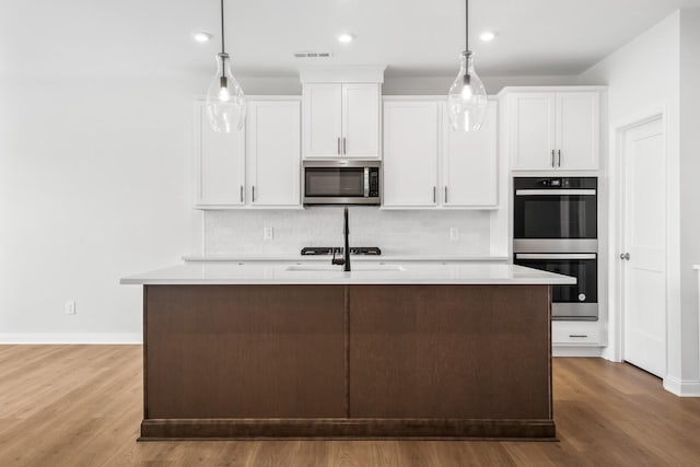 kitchen with stainless steel appliances, hanging light fixtures, a center island with sink, and white cabinets