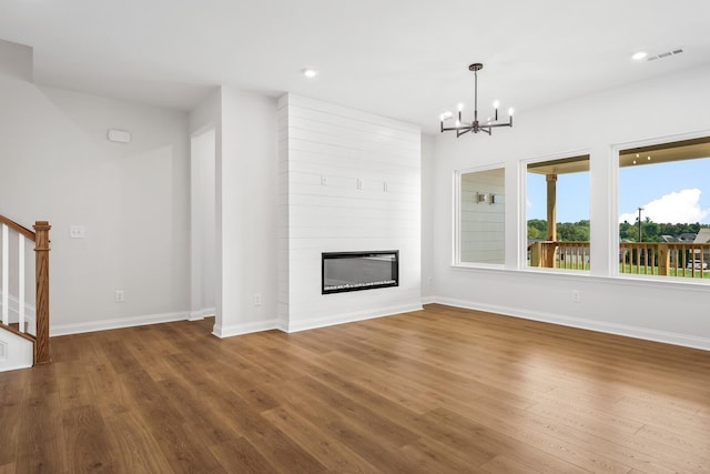 unfurnished living room with a notable chandelier, a fireplace, wood finished floors, visible vents, and stairway