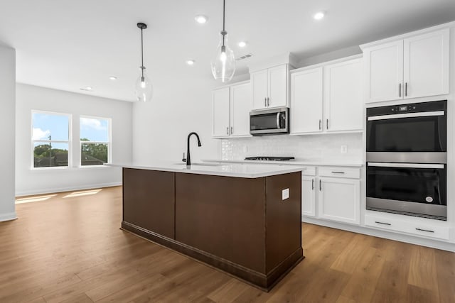 kitchen featuring a sink, white cabinets, light countertops, hanging light fixtures, and stainless steel microwave