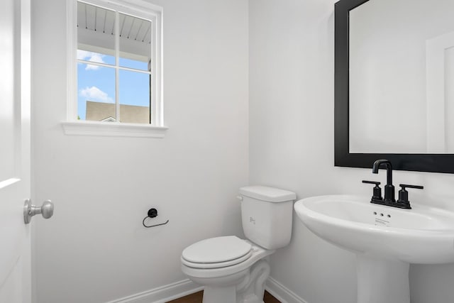 half bath with baseboards, a sink, and toilet