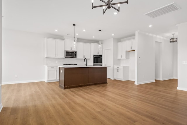 kitchen with a center island with sink, stainless steel appliances, light countertops, visible vents, and white cabinets