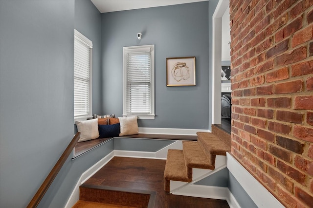 interior space with wood finished floors, brick wall, baseboards, and stairs