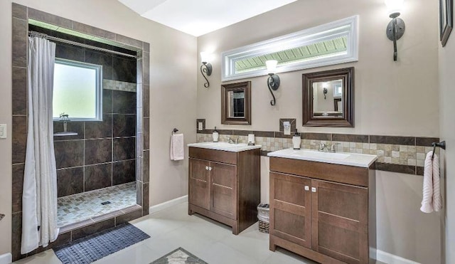 full bath featuring tiled shower, two vanities, a sink, and tile walls