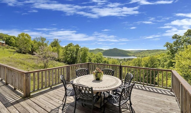 deck featuring a forest view, outdoor dining area, and a water and mountain view