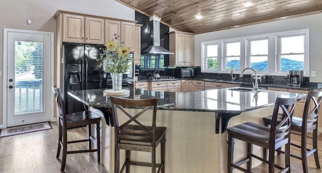 kitchen with a sink, wood ceiling, wall chimney range hood, light wood-type flooring, and dark stone countertops