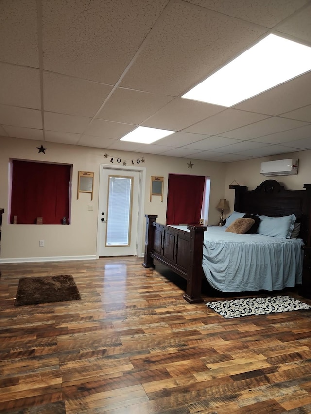 bedroom with a paneled ceiling, a wall mounted air conditioner, baseboards, and wood finished floors