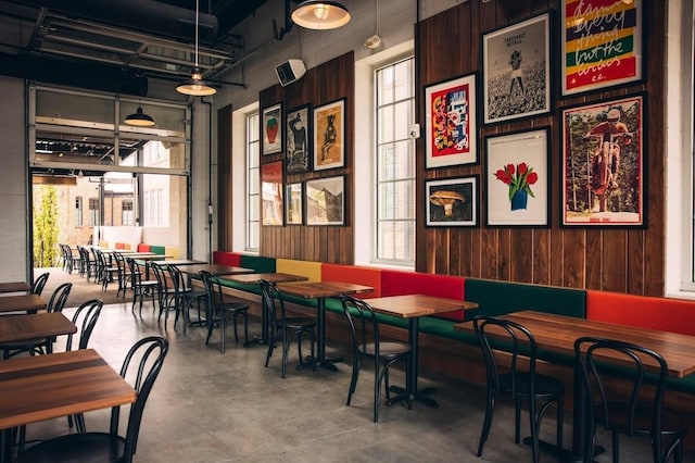 dining area featuring plenty of natural light, concrete floors, wooden walls, and a high ceiling