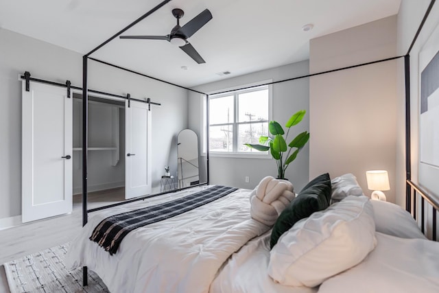 bedroom with light wood-type flooring, a barn door, visible vents, and ceiling fan