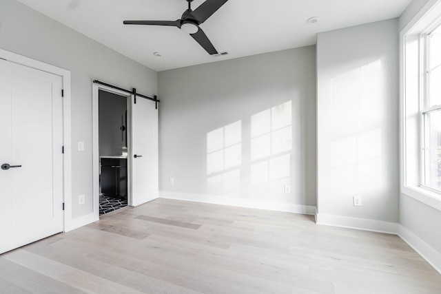 unfurnished bedroom with light wood finished floors, a barn door, connected bathroom, and baseboards