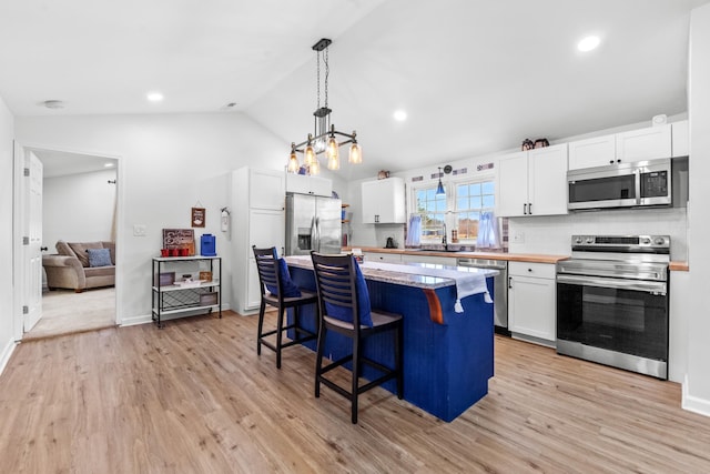 kitchen featuring appliances with stainless steel finishes, a center island, decorative light fixtures, a kitchen bar, and white cabinetry