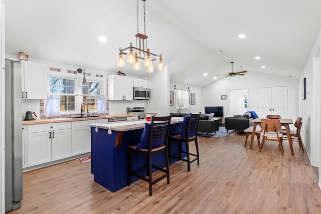 kitchen with stainless steel appliances, open floor plan, white cabinets, and decorative light fixtures