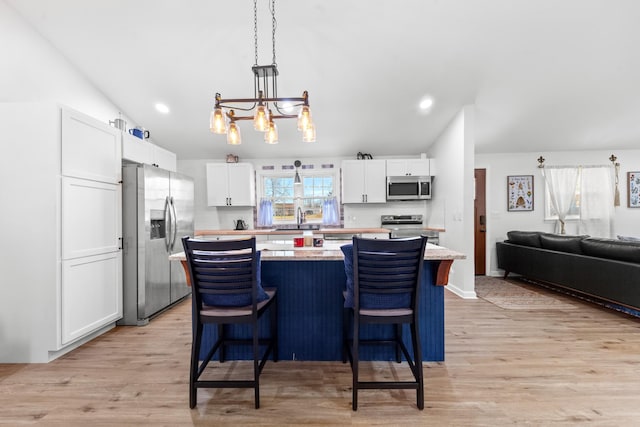 kitchen with stainless steel appliances, a kitchen island, a sink, white cabinetry, and a kitchen bar