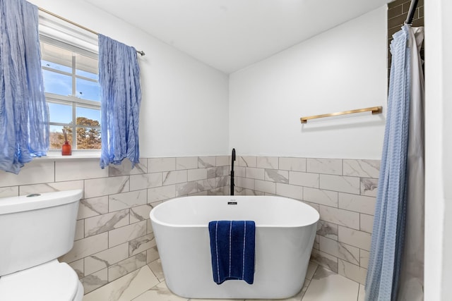 full bath with toilet, a soaking tub, marble finish floor, and a wainscoted wall