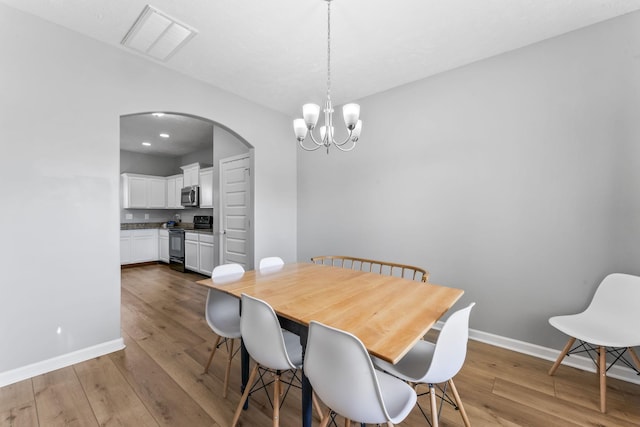 dining space featuring baseboards, visible vents, arched walkways, and hardwood / wood-style floors