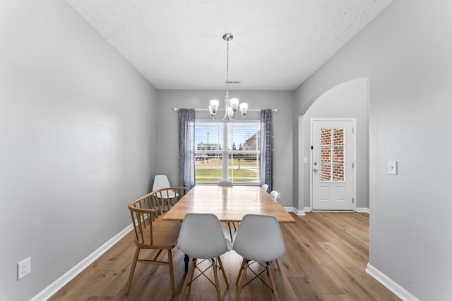 dining room featuring arched walkways, baseboards, hardwood / wood-style floors, and an inviting chandelier