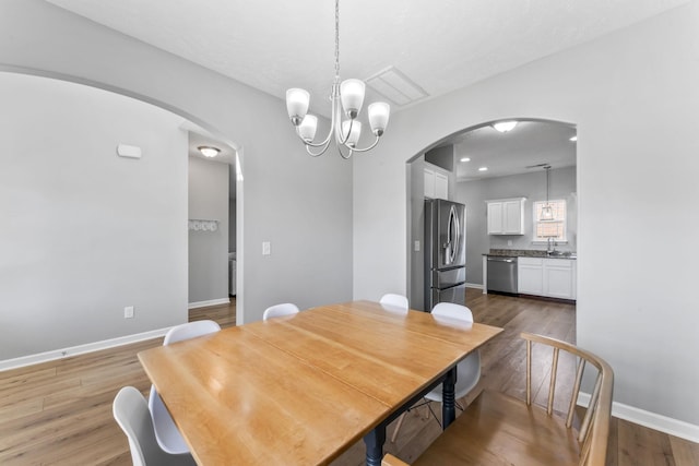 dining space with arched walkways, an inviting chandelier, wood finished floors, and baseboards