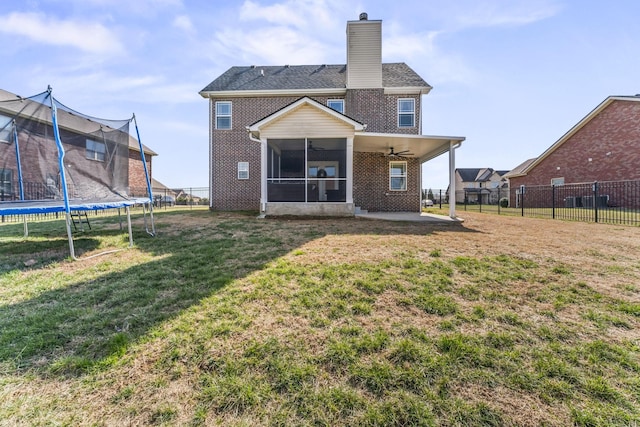 back of house featuring a trampoline, brick siding, a yard, and a chimney