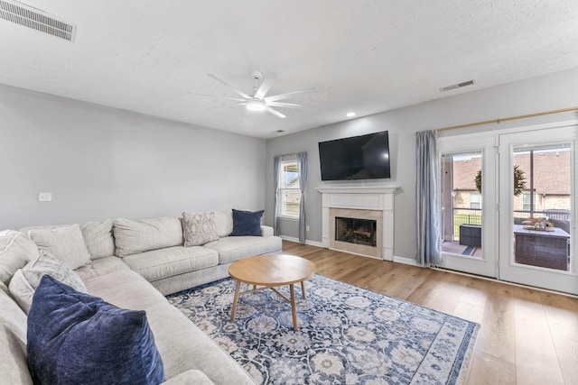 living room with ceiling fan, wood finished floors, visible vents, and a high end fireplace