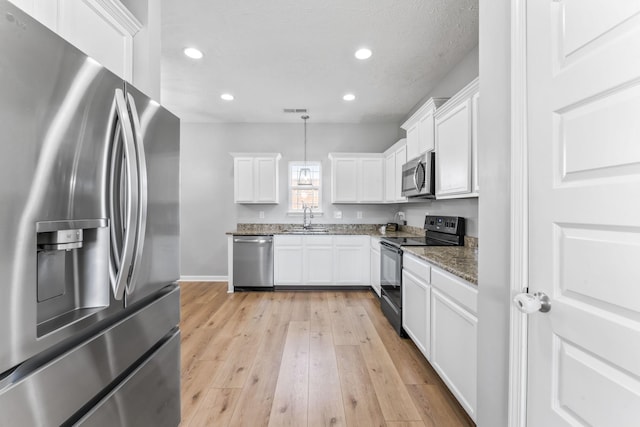 kitchen featuring stainless steel appliances, light wood-style floors, white cabinetry, a sink, and dark stone counters