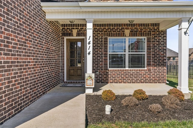 view of exterior entry featuring a porch and brick siding