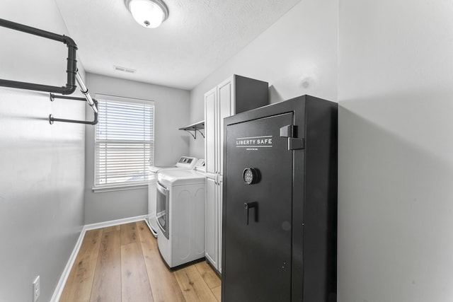 washroom with light wood-style flooring, visible vents, baseboards, cabinet space, and washer and clothes dryer