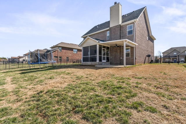 back of property featuring a trampoline, a sunroom, brick siding, and a yard