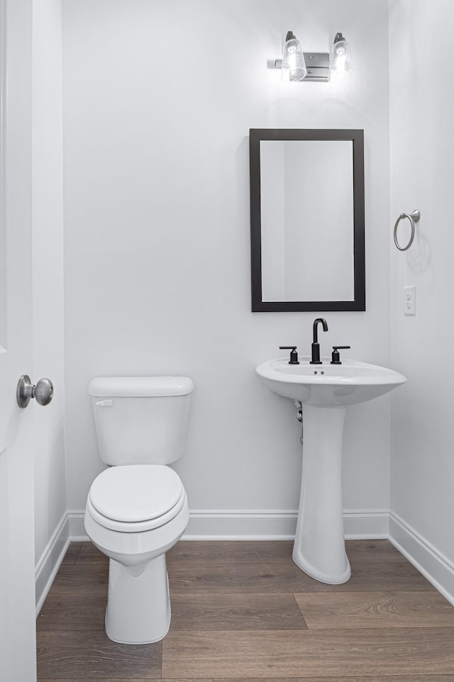 half bath with a sink, wood finished floors, toilet, and baseboards