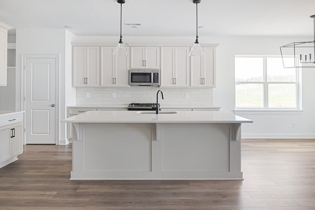 kitchen with a center island with sink, stainless steel microwave, hanging light fixtures, light countertops, and a sink