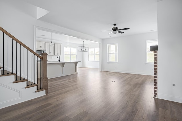 unfurnished living room with ceiling fan, dark wood-type flooring, a sink, baseboards, and stairway