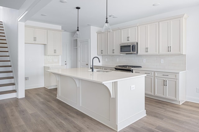 kitchen with appliances with stainless steel finishes, a kitchen island with sink, light countertops, and a sink