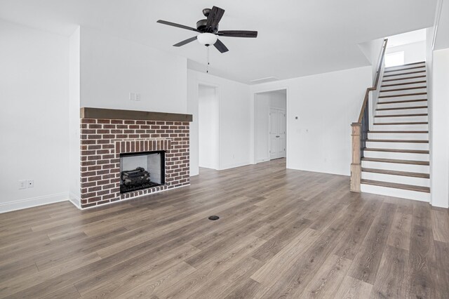 unfurnished living room with stairs, a fireplace, ceiling fan, and wood finished floors