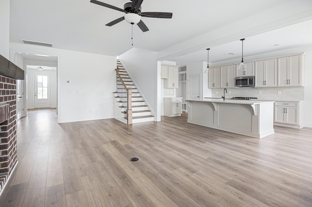 unfurnished living room with ceiling fan, a sink, visible vents, light wood-style floors, and stairway