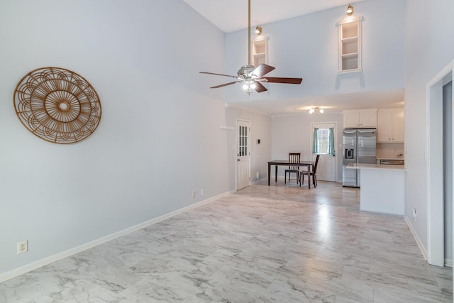 unfurnished living room featuring marble finish floor, a high ceiling, ceiling fan, and baseboards