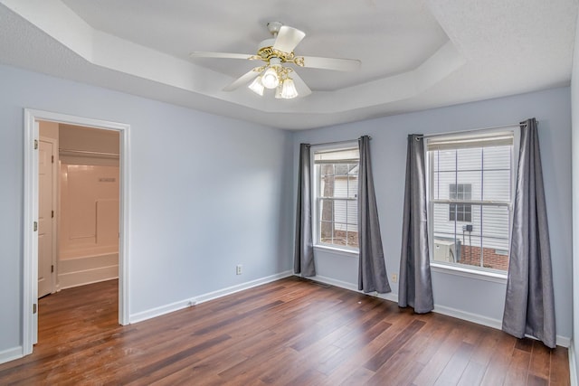 empty room with dark wood-style floors, ceiling fan, a raised ceiling, and baseboards