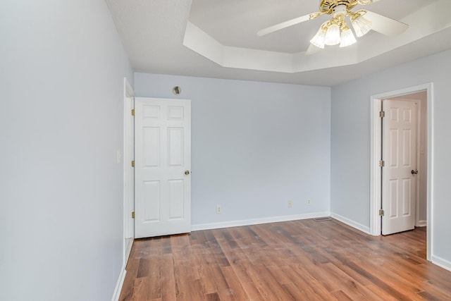 unfurnished room featuring a ceiling fan, a raised ceiling, baseboards, and wood finished floors