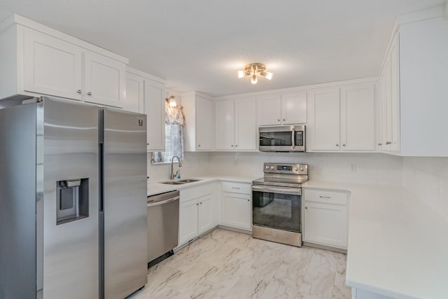 kitchen featuring marble finish floor, appliances with stainless steel finishes, white cabinets, and a sink