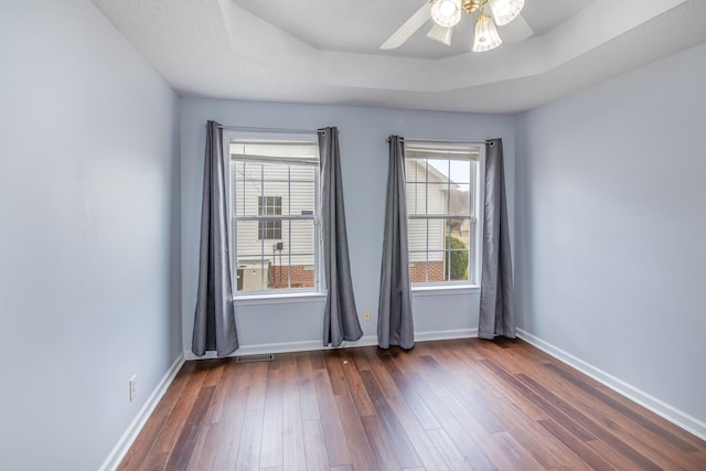 spare room featuring baseboards, visible vents, a ceiling fan, dark wood-type flooring, and a tray ceiling