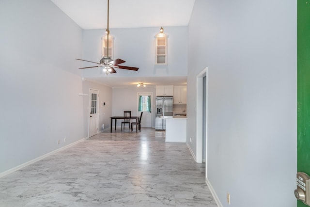 unfurnished living room with a ceiling fan, marble finish floor, a towering ceiling, and baseboards