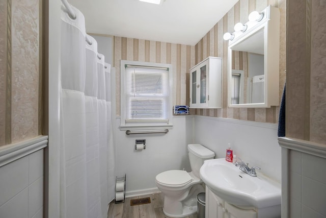 full bath with a wainscoted wall, toilet, vanity, wood finished floors, and wallpapered walls