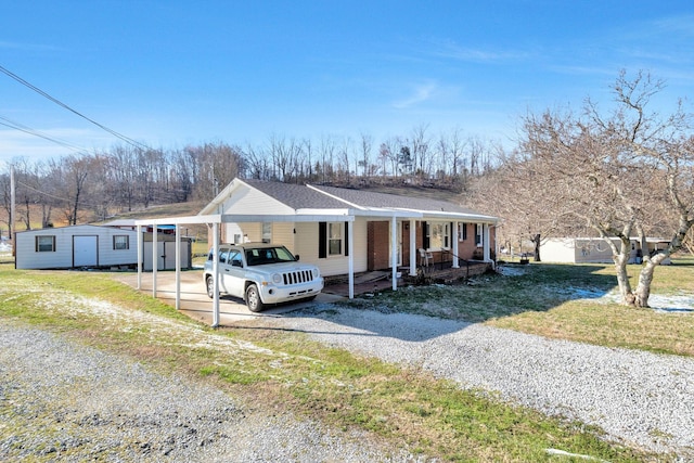 view of front of home with a porch, an outdoor structure, a carport, a front lawn, and gravel driveway