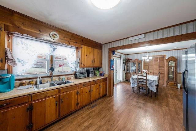 kitchen with brown cabinetry, freestanding refrigerator, light countertops, pendant lighting, and a sink