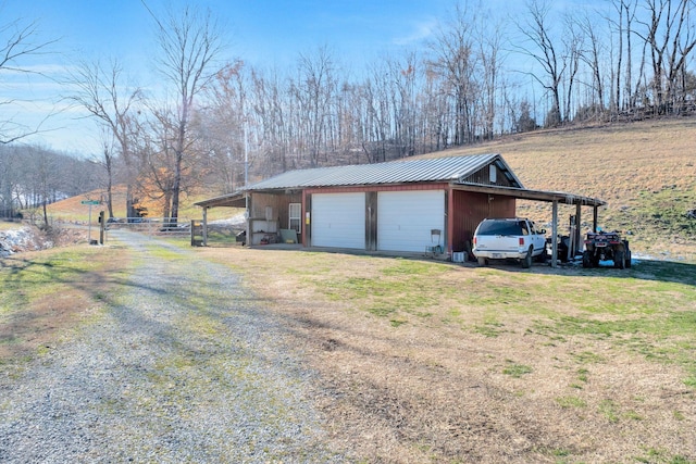 view of side of property featuring a garage, driveway, metal roof, an outbuilding, and a yard