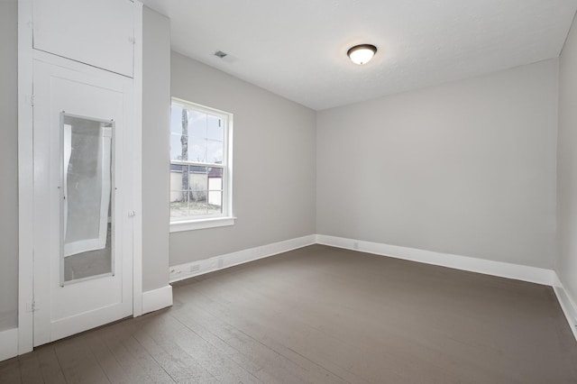 unfurnished room with visible vents, dark wood finished floors, and baseboards