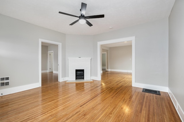 unfurnished living room featuring a brick fireplace, wood finished floors, visible vents, and baseboards