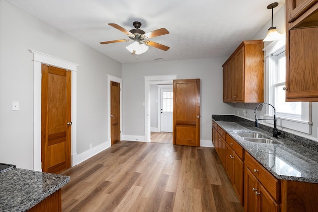 kitchen featuring a sink, light wood-type flooring, a wealth of natural light, brown cabinetry, and decorative light fixtures