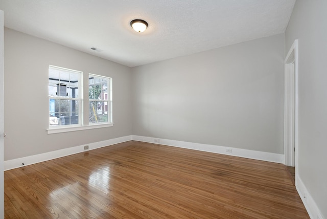 unfurnished room with a textured ceiling, wood finished floors, visible vents, and baseboards