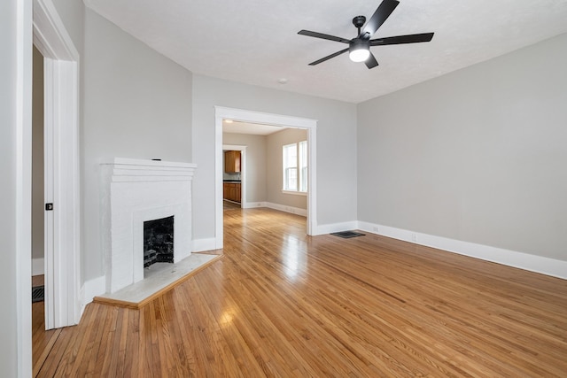 unfurnished living room with a fireplace with raised hearth, ceiling fan, visible vents, baseboards, and light wood-type flooring