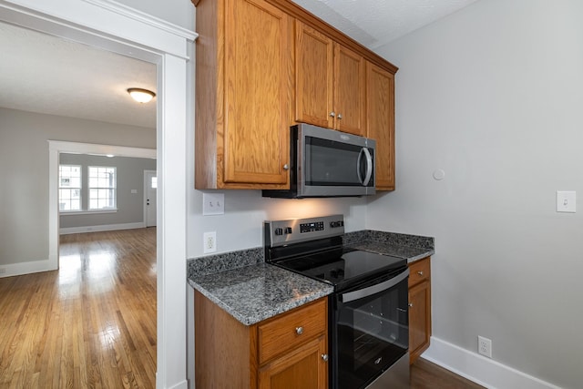 kitchen featuring appliances with stainless steel finishes, baseboards, brown cabinets, and dark stone countertops