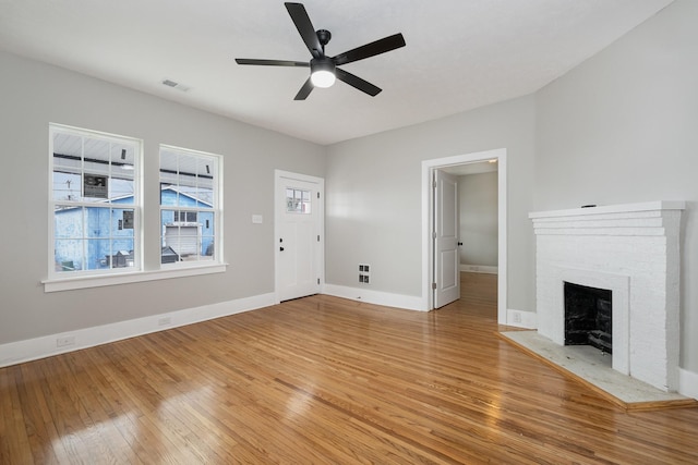 unfurnished living room featuring a brick fireplace, visible vents, baseboards, and wood finished floors