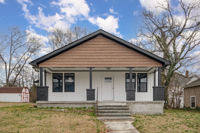 bungalow-style home with a front yard, covered porch, an outdoor structure, and a storage unit